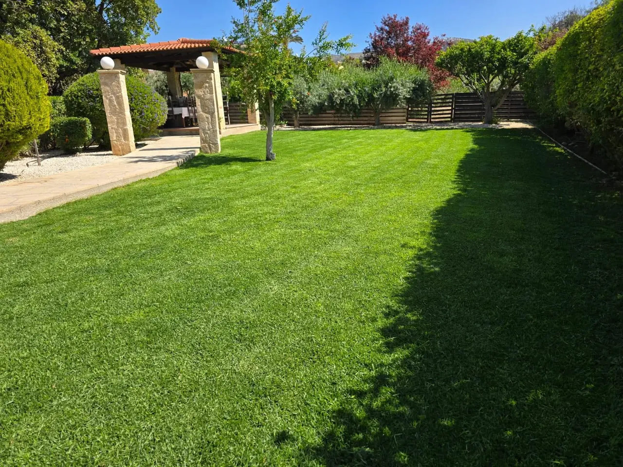 Freshly mown lawn in late sun beside a stone pergola
